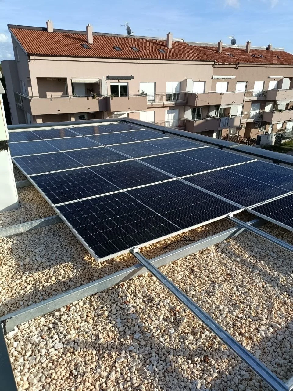 Solarni paneli na ravnom šljunčanom krovu, sa stambenom zgradom u pozadini.