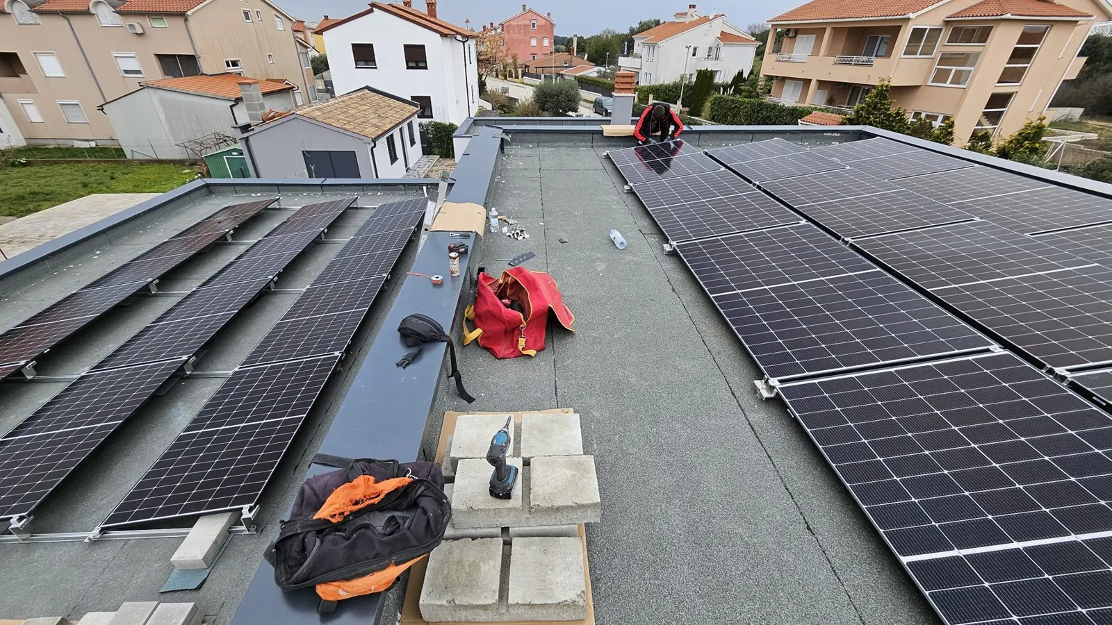 Monteri na ravnom krovu tijekom postavljanja solarnih panela, s alatom i opremom u prvom planu.